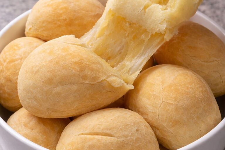 Vários pães de queijo veganos, redondos, um está esticado mostrando a sua elasticidade.
