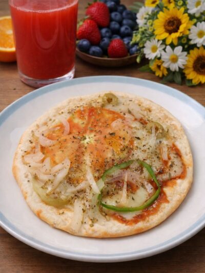 pizza redonda em um prato. a pizza tem tomate, cebola, pimentão, queijo vegano, molho de tomate e orégano.